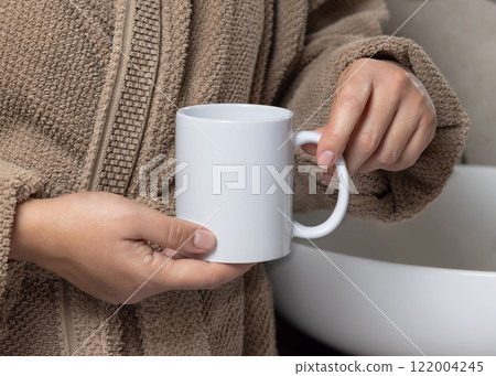 Woman in brown bathrobe holding white blank coffee mug against basin closeup,  mockup 122004245