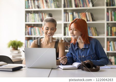 Smiling girls students use laptop for online studying at library Smiling girls students use laptop for online studying at library 122004263