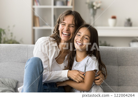 Laughing mother cuddling her little daughter seated on cozy couch Laughing mother cuddling her little daughter seated on cozy couch 122004264