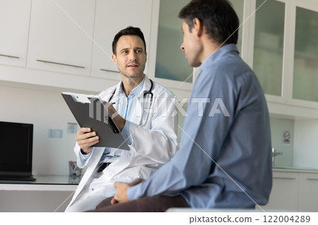 Caring young male doctor meeting with patient in clinic room 122004289