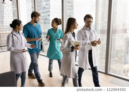 Diverse doctors actively talking while walking through hallway Diverse doctors actively talking while walking through hallway 122004302