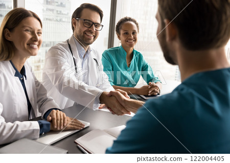 Diverse medical workers shaking hands at conference table Diverse medical workers shaking hands at conference table 122004405