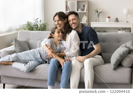 Hispanic couple and little 6s daughter laughing seated on couch 122004410