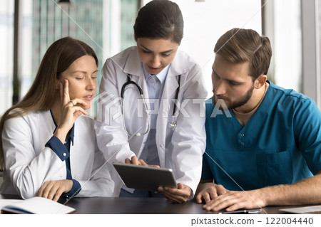 Doctors examining information on tablet at meeting in clinic 122004440