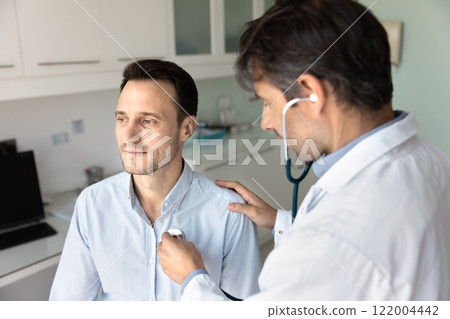 Serious clinic cardiologist doctor examining man, applying stethoscope to chest 122004442