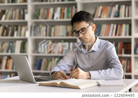 Serious motivated young male student taking notes at library desk 122004495