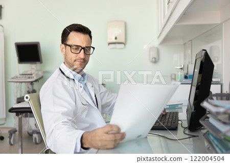 Serious young doctor man reading paper medical report 122004504