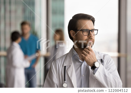 Thoughtful doctor deep in thought standing in clinic office Thoughtful doctor deep in thought standing in clinic office 122004512