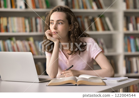Pensive female student sit at library desk look aside ponder Pensive female student sit at library desk look aside ponder 122004544