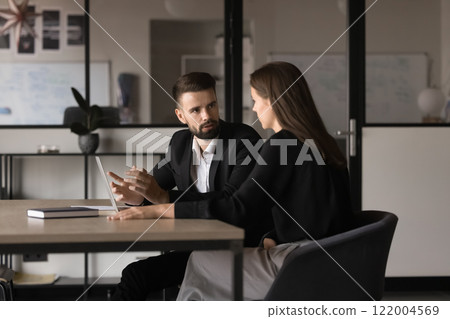 Two young Caucasian teammates involved in dialogue in meeting room 122004569