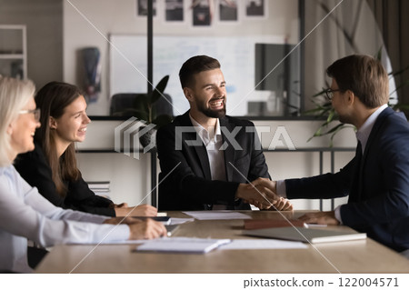 Two smiling millennial businessmen closing deal and shaking hands 122004571
