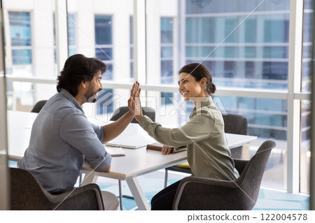Two happy young Indian colleagues giving high five symbolizing cooperation Two happy young Indian colleagues giving high five symbolizing cooperation 122004578