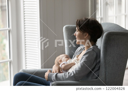 Happy woman sit in armchair look at window breastfeeding baby 122004826