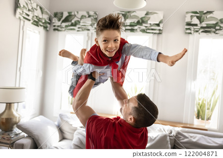 Strong caring father lifting cheerful son wearing superhero cape overhead 122004871
