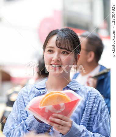 A woman eating the famous takosen (octopus crackers) as she walks through Dotonbori, Osaka 122004928