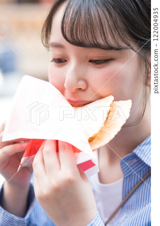 A woman eating the famous takosen (octopus crackers) as she walks through Dotonbori, Osaka 122004935