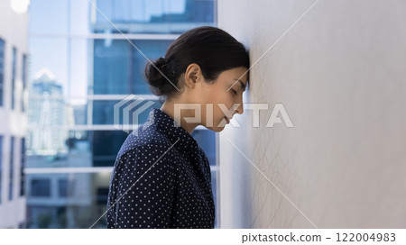 Stressed tired young Indian employee woman banging head against wall 122004983