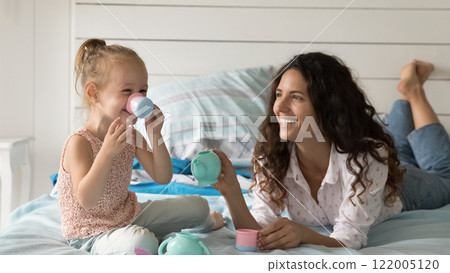 Young mom little girl play toy tea set on bed 122005120