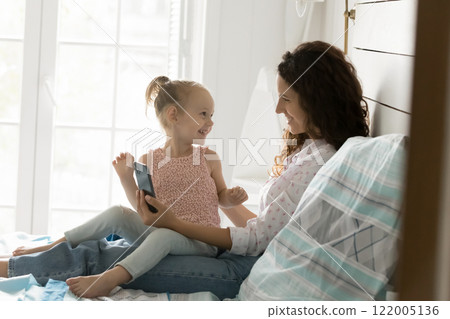 Happy mom daughter preschooler sit on bed chat use phone 122005136