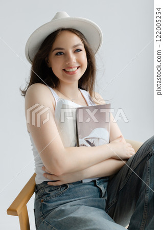 Young woman reading magazine sitting on chair Young woman reading magazine sitting on chair 122005254