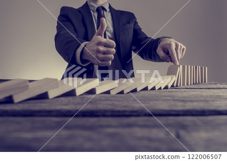 Businessman in business suit stopping dominoes row from crumbling 122006507