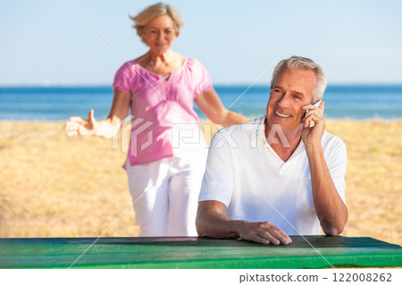 Happy Senior Couple Man talking on a Cell Phone Woman Running Behind him Happy Senior Couple Man talking on a Cell Phone Woman Running Behind him 122008262