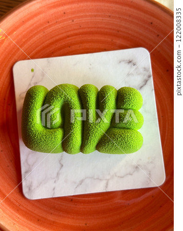 Bright green mousse dessert shaped like the word LOVE is displayed on a vibrant orange plate. Artistic and appetizing presentation. Valentines day concept Bright green mousse dessert shaped like the word LOVE is displayed on a vibrant orange plate. Artistic and appetizing presentation. Valentines day concept 122008335