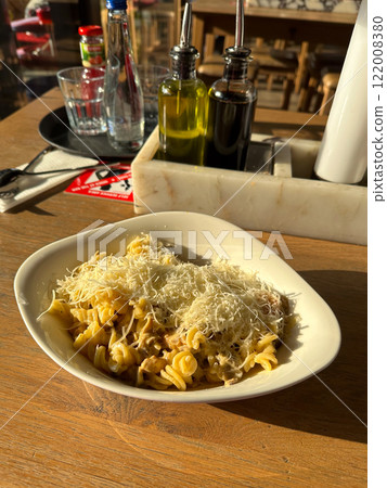Bowl of pasta topped generously with grated cheese under warm sunlight. Rustic wooden table adds to the inviting and homely atmosphere Bowl of pasta topped generously with grated cheese under warm sunlight. Rustic wooden table adds to the inviting and homely atmosphere 122008380