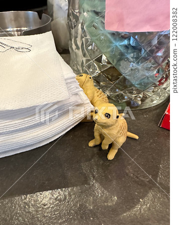 Small meerkat figurines sitting beside folded napkins on a cafe counter. A charming detail adds personality to a casual coffee shop setting Small meerkat figurines sitting beside folded napkins on a cafe counter. A charming detail adds personality to a casual coffee shop setting 122008382