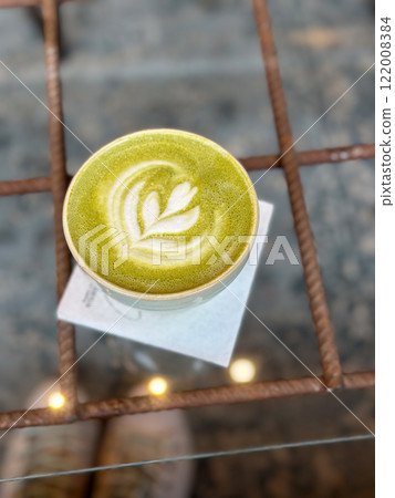 Cup of vibrant green matcha latte with artistic foam design captured from above. Creating a cozy and inviting mood in coffee shop 122008384