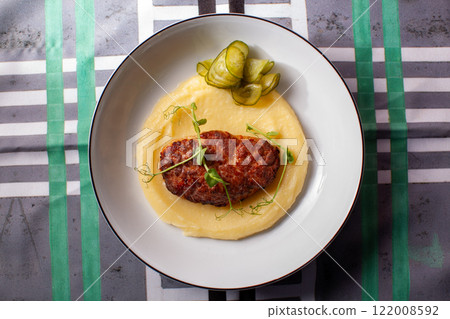 Chicken Kiev cutlet served on a bed of mashed potatoes with pickles and microgreens, presented on a white plate with a modern tablecloth Chicken Kiev cutlet served on a bed of mashed potatoes with pickles and microgreens, presented on a white plate with a modern tablecloth 122008592