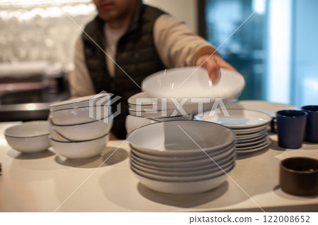 Waiter arranging white plates and bowls on a restaurant table, preparing for customers, russian cuisine Waiter arranging white plates and bowls on a restaurant table, preparing for customers, russian cuisine 122008652