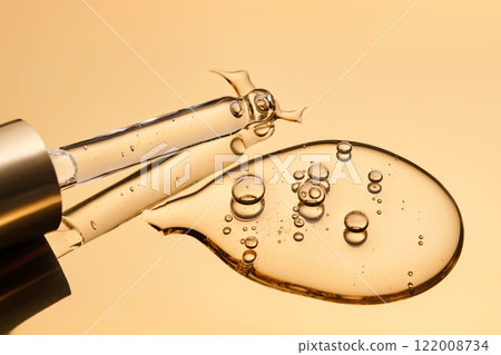 A beautiful drop of gel-like cosmetic serum with bubbles on a golden background. 122008734