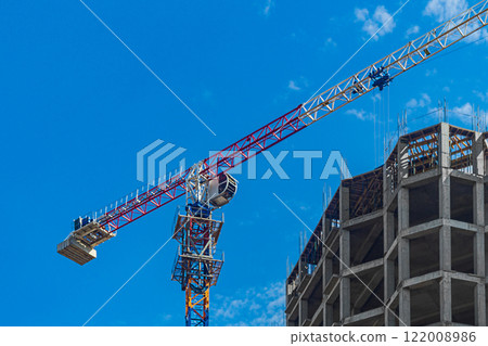 Construction crane, multi-story building under construction in process of erecting load-bearing elements of frame made of monolithic reinforced concrete on sky background. House building industry Construction crane, multi-story building under construction in process of erecting load-bearing elements of frame made of monolithic reinforced concrete on sky background. House building industry 122008986