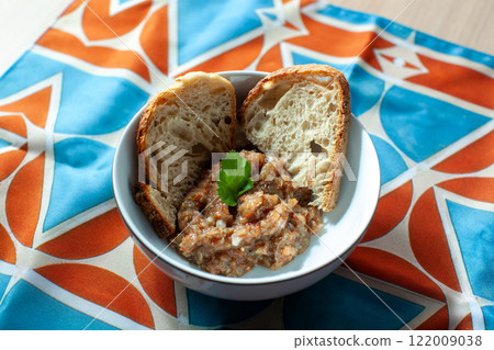 Bowl of eggplant caviar, also known as aubergine caviar, served with two slices of bread and garnished with a coriander leaf, placed on a colorful tablecloth 122009038