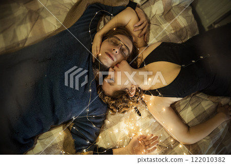 Romantic moment between a loving couple surrounded by fairy lights in a cozy setting Romantic moment between a loving couple surrounded by fairy lights in a cozy setting 122010382