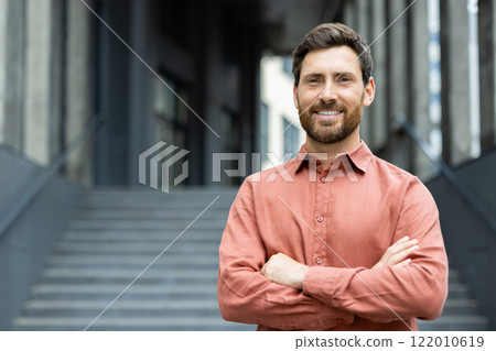 Portrait of confident and successful businessman outside office building. Man in red shirt smiling and looking at camera with arms crossed. Portrait of confident and successful businessman outside office building. Man in red shirt smiling and looking at camera with arms crossed. 122010619