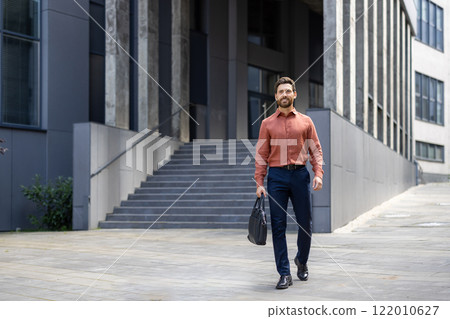 A successful businessman in full growth walks through the city with a business bag in his hands, a mature man smiles contentedly from outside an office building. 122010627