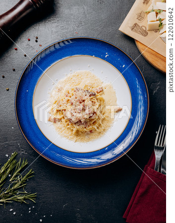 Classic Italian pasta carbonara served on an elegant blue plate with parmesan and creamy sauce 122010642