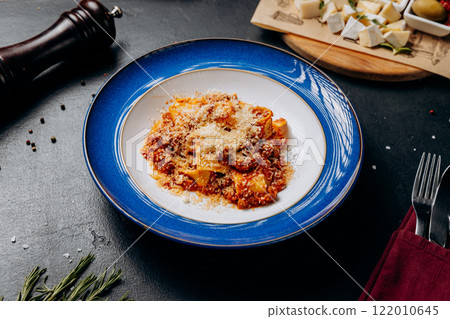 Authentic Italian pappardelle bolognese topped with parmesan cheese on a classic blue plate 122010645