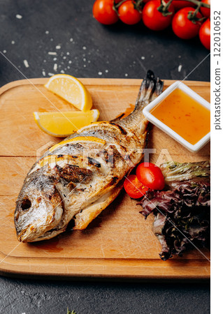 Grilled fish served with fresh salad, lemon wedges, and dipping sauce on a wooden platter Grilled fish served with fresh salad, lemon wedges, and dipping sauce on a wooden platter 122010652