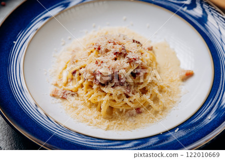 Classic Italian pasta carbonara served on an elegant blue plate with parmesan and creamy sauce 122010669