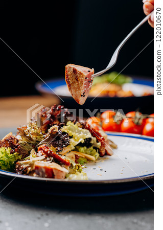 Fork lifting seared tuna over fresh salad, a perfect blend of healthy and gourmet dining 122010670