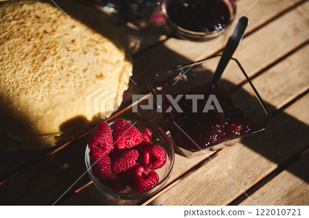 Delicious pancakes with raspberries and jam on a sunny wooden table Delicious pancakes with raspberries and jam on a sunny wooden table 122010721