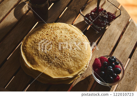 Stack of pancakes served with berries and jam on a wooden table Stack of pancakes served with berries and jam on a wooden table 122010723