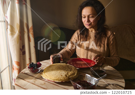 Woman enjoying pancakes and fruits during a cozy morning indoors 122010725