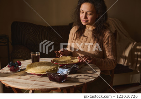 Woman enjoying pancakes with spread and fruit at a cozy kitchen table Woman enjoying pancakes with spread and fruit at a cozy kitchen table 122010726