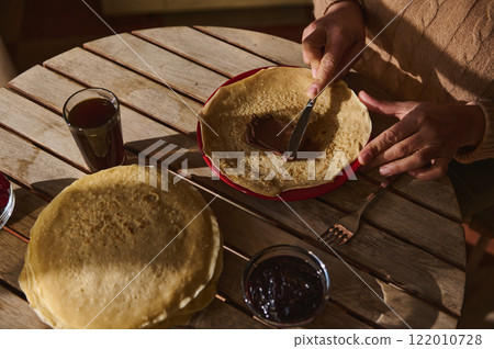 Hands spreading chocolate on pancakes with jam and drinks for a tasty treat 122010728