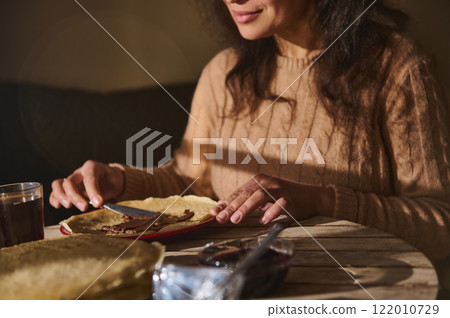 Person spreading chocolate on crepes in a cozy setting 122010729