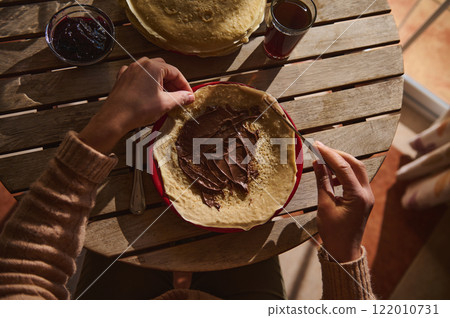 Person Preparing a Crepe with Chocolate Spread at a Wooden Table 122010731